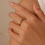 Close-up of a hand wearing a gold ring with a heart-shaped gemstone on a beige background